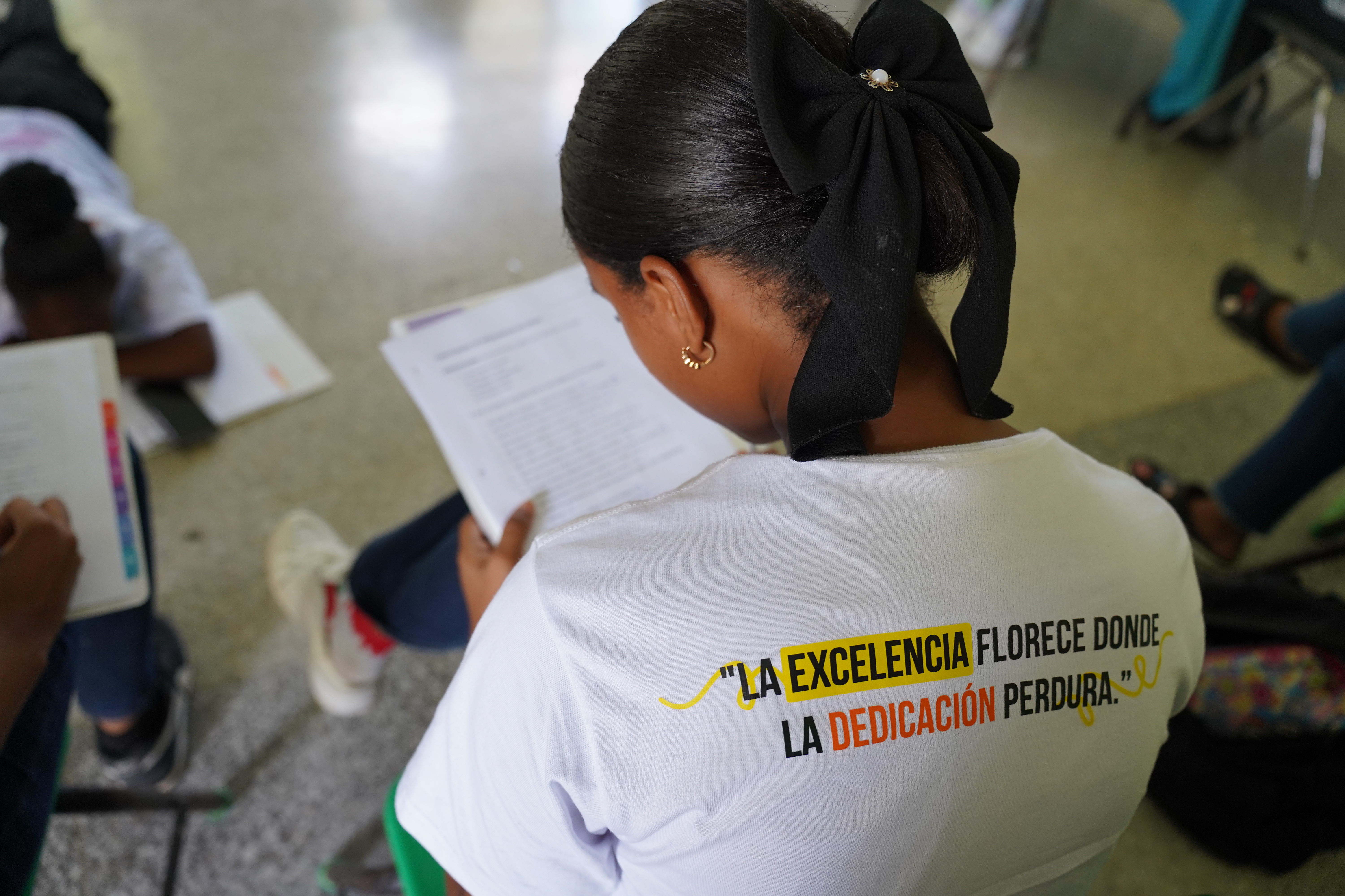 A young woman seen from the back, reading a document in a classroom.