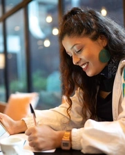 Young woman smiling as she writes down notes while holding an iPad