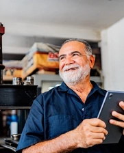 Image of a senior man smiling and holding a tablet while working at his workshop