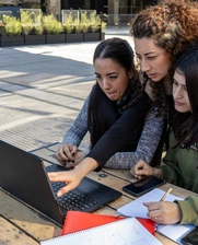 A group of three female students looking at a laptop in an outdoor park