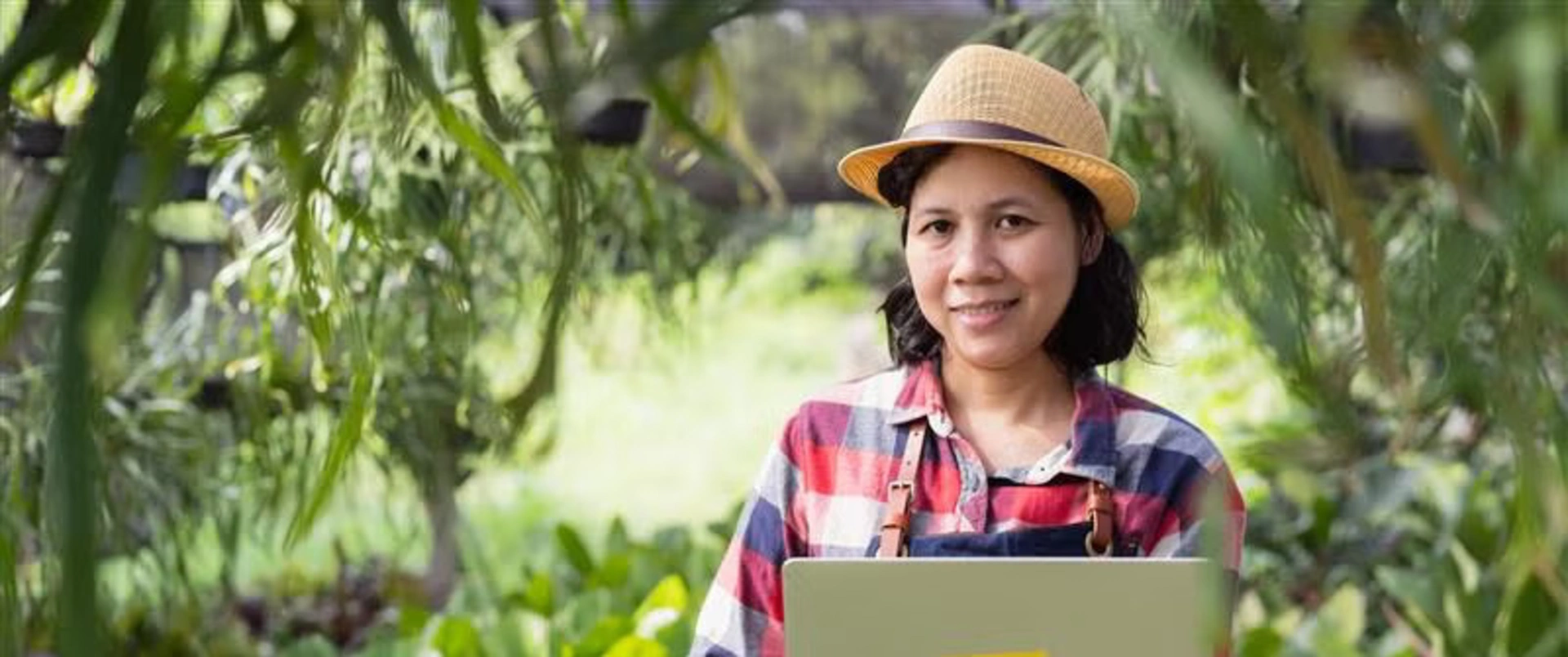 Banner image of a woman working at a crop while she holds her laptop