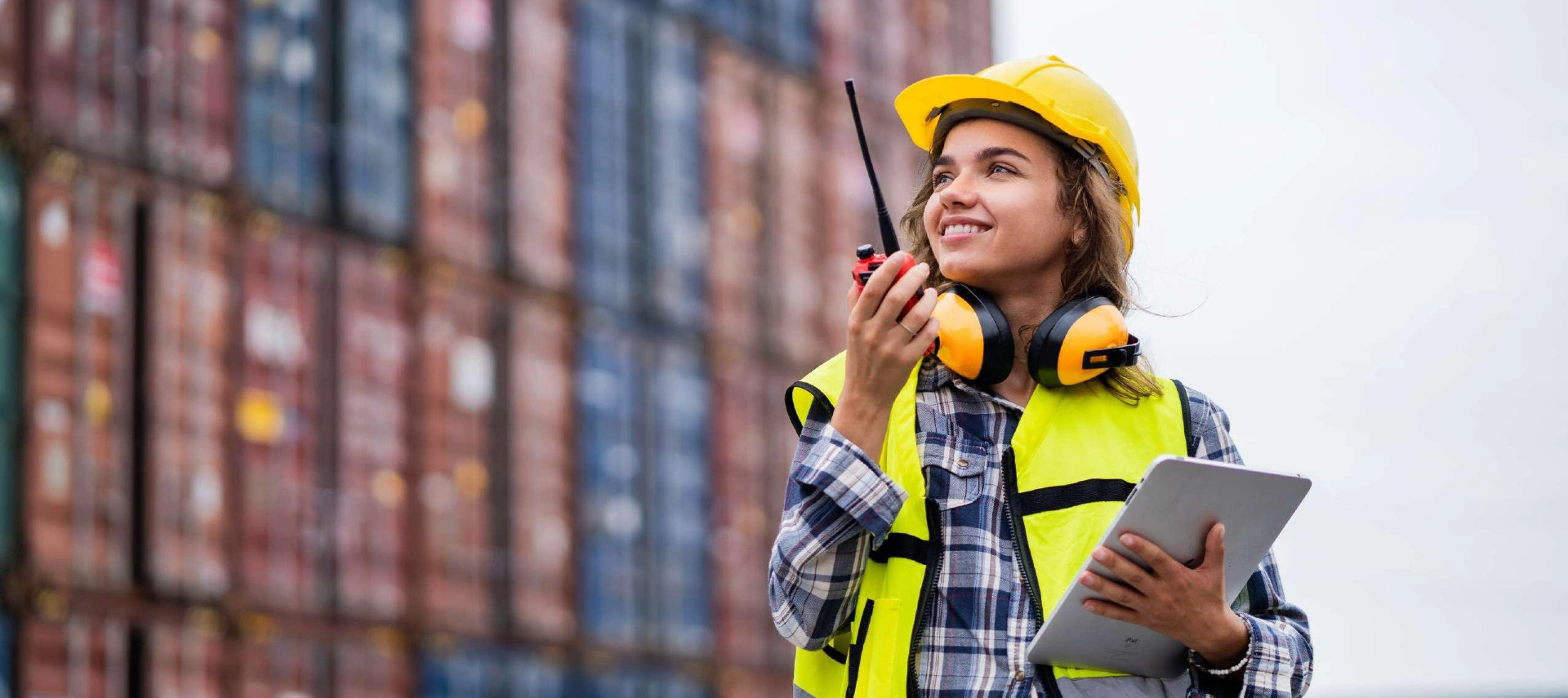 Image of a young woman working at a port dock with containers behind her