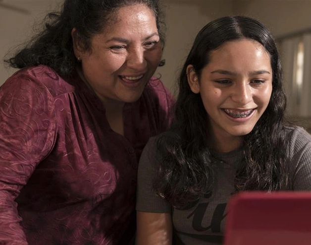 A mother and a daughter looking at a tablet and smiling 