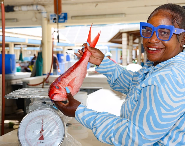 A female worker in a fish shop in Barbados, showing a flying fish, smiling at camera 