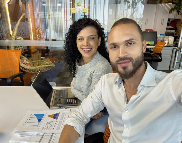 Dos personas sentadas en un escritorio con computadoras portátiles, colaborando en un espacio de trabajo.