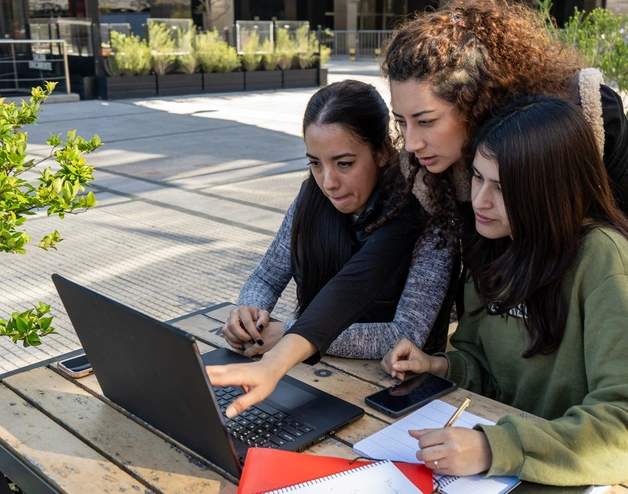 A group of three female students looking at a laptop in an outdoor park