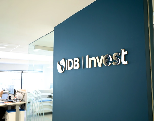 IDB Invest logo displayed on a blue wall in an office