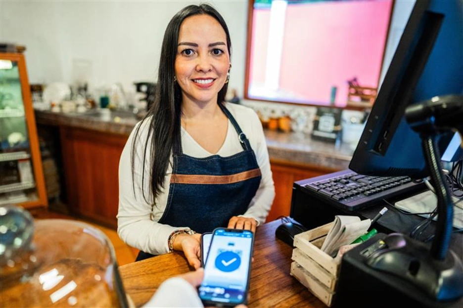 A woman in a commercial shop holds an electronic payment reader.