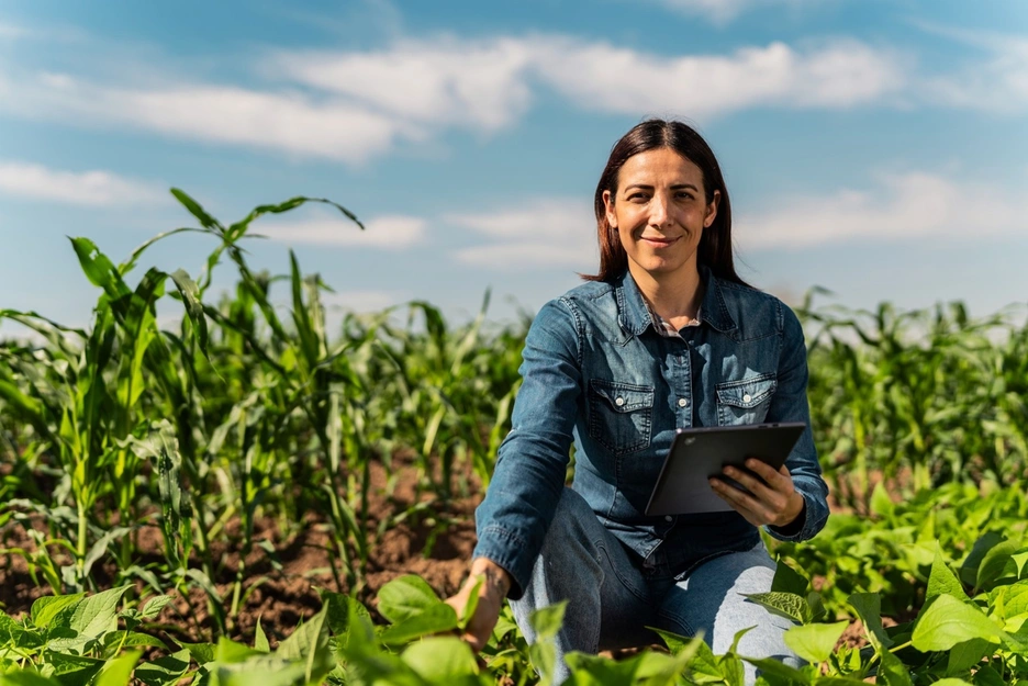 Mulher em um campo de cultivo usando plataformas digitais para a produção agrícola.
