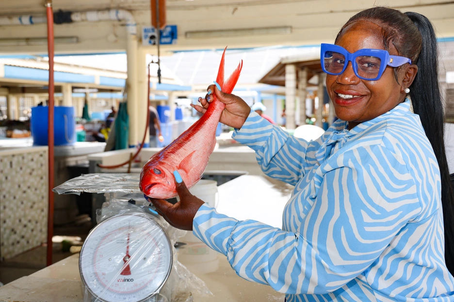 A female worker in a fish shop in Barbados, showing a flying fish, smiling at camera 