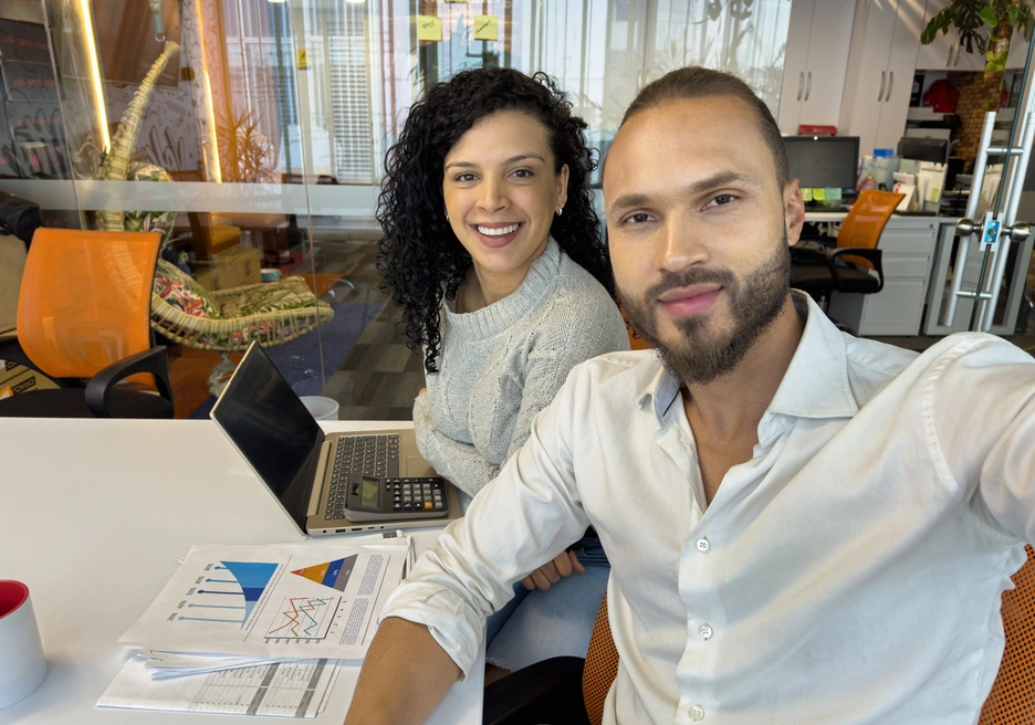 Dos personas sentadas en un escritorio con computadoras portátiles, colaborando en un espacio de trabajo.