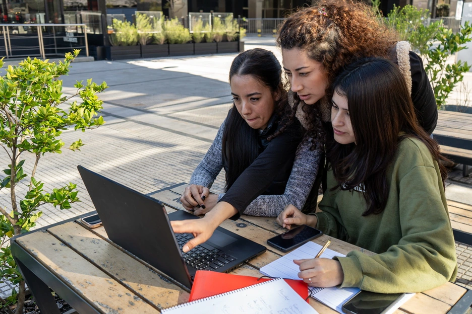 A group of three female students looking at a laptop in an outdoor park